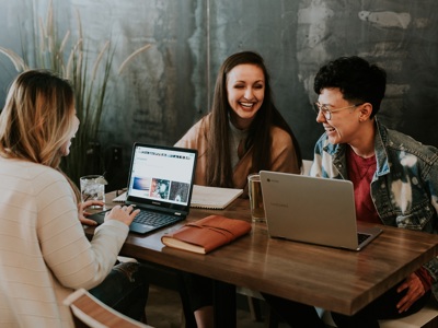 three people sitting  around a table smiling 